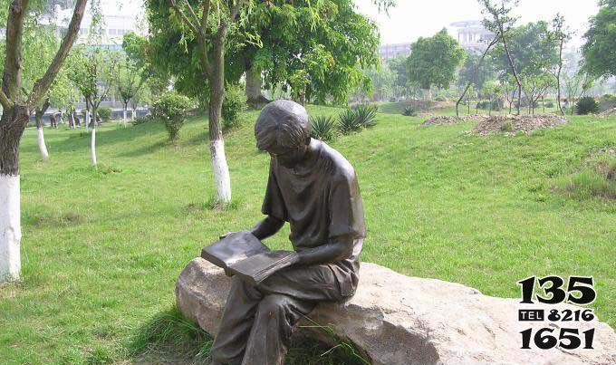 讀書雕塑-公園草坪玻璃鋼仿銅坐著石頭上的男孩讀書雕塑高清圖片